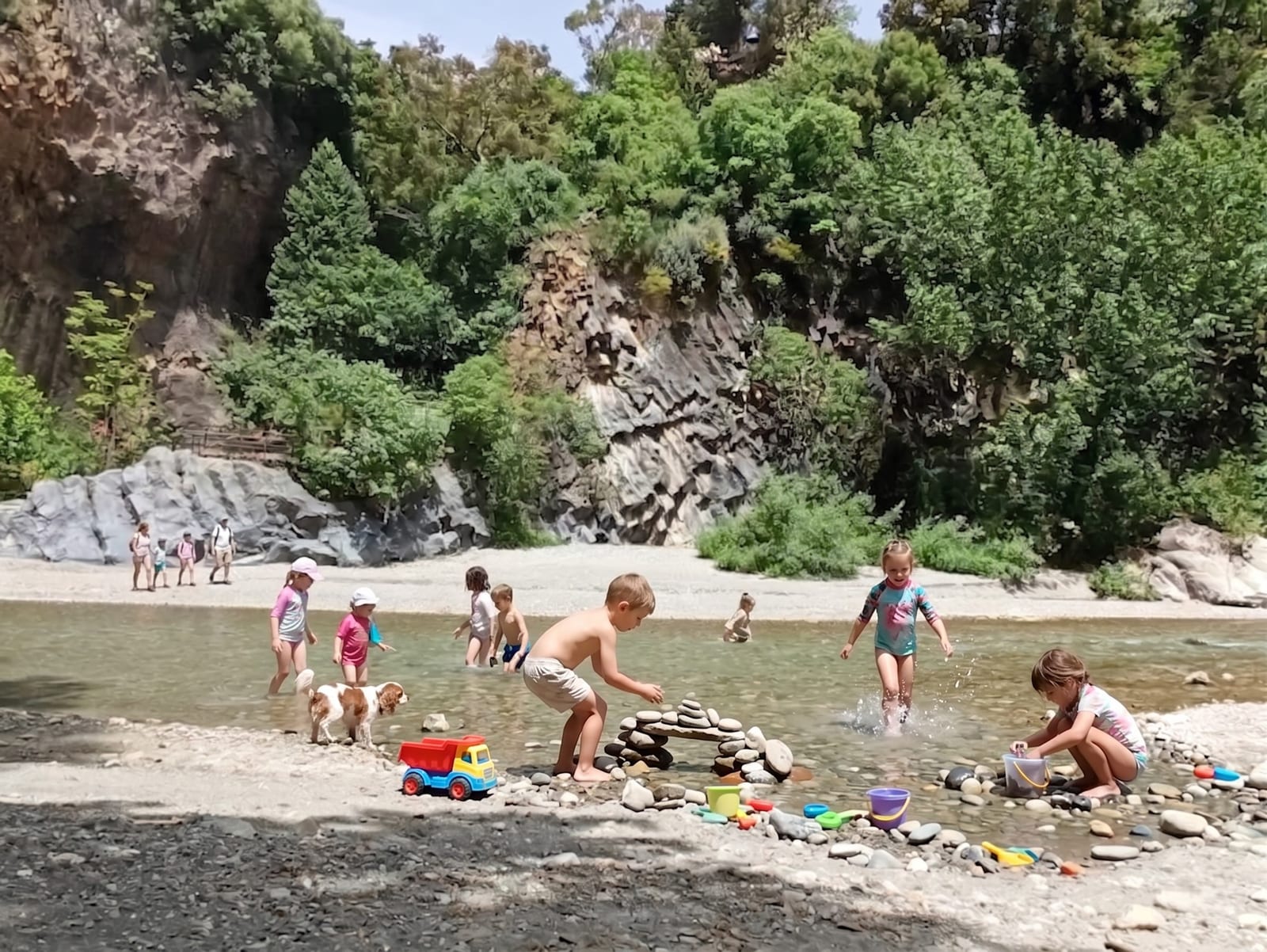 Bambini che giocano nel fiume Alcantara con secchielli e formine, pareti basaltiche delle gole sullo sfondo
